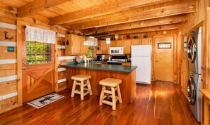 A wooden cabin interior with a kitchen, wooden stools, a refrigerator, and a washing machine. - Hard to Leave - Stunning Mountain Views, Pool Table, Games, Hot Tub! (Sevierville)