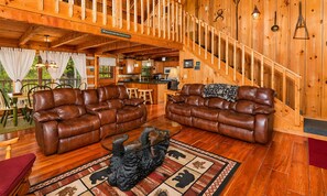 A wooden interior with two leather sofas, a dining area, and a staircase. - Hard to Leave - Stunning Mountain Views, Pool Table, Games, Hot Tub! (Sevierville)