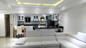 Ein modernes Wohnzimmer mit Ecksofa, Couchtisch und Küchenbereich mit weißen Schränken und einer schwarzen Arbeitsplatte.