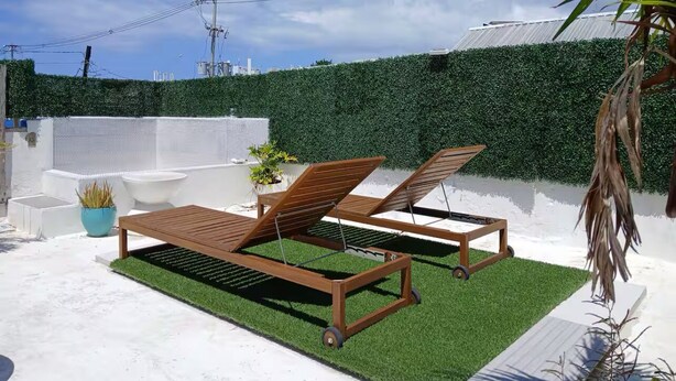 Eine Dachterrasse mit zwei Holzliegen, einem kleinen Tisch und einem Blumentopf.