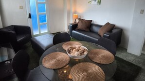 Ein modernes Wohnzimmer mit einem Glastisch, einer schwarzen Ledersofa und gewebten Untersetzern.