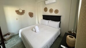 Ein ordentlich eingerichtetes Schlafzimmer mit einem Bett, einem Nachttisch, einer Wand-Klimaanlage und einem kleinen Korb.