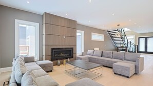 Ein modernes Wohnzimmer mit einem Ecksofa, einem Flachbildfernseher, einem Kamin und einer Treppe.