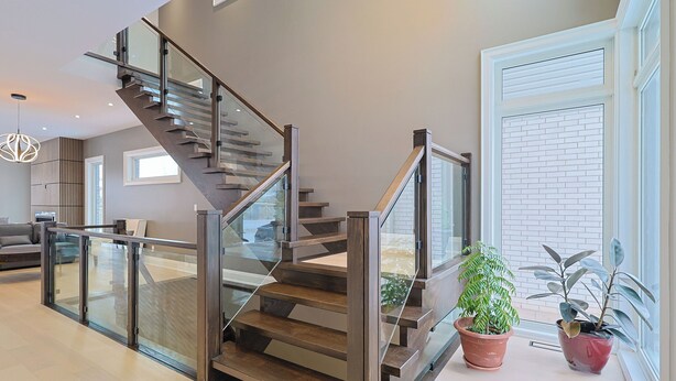 Eine moderne Treppe mit Glastrennwand und Holzbeschlägen, die zu einer Podestebene mit Pflanzgefäßen führt.