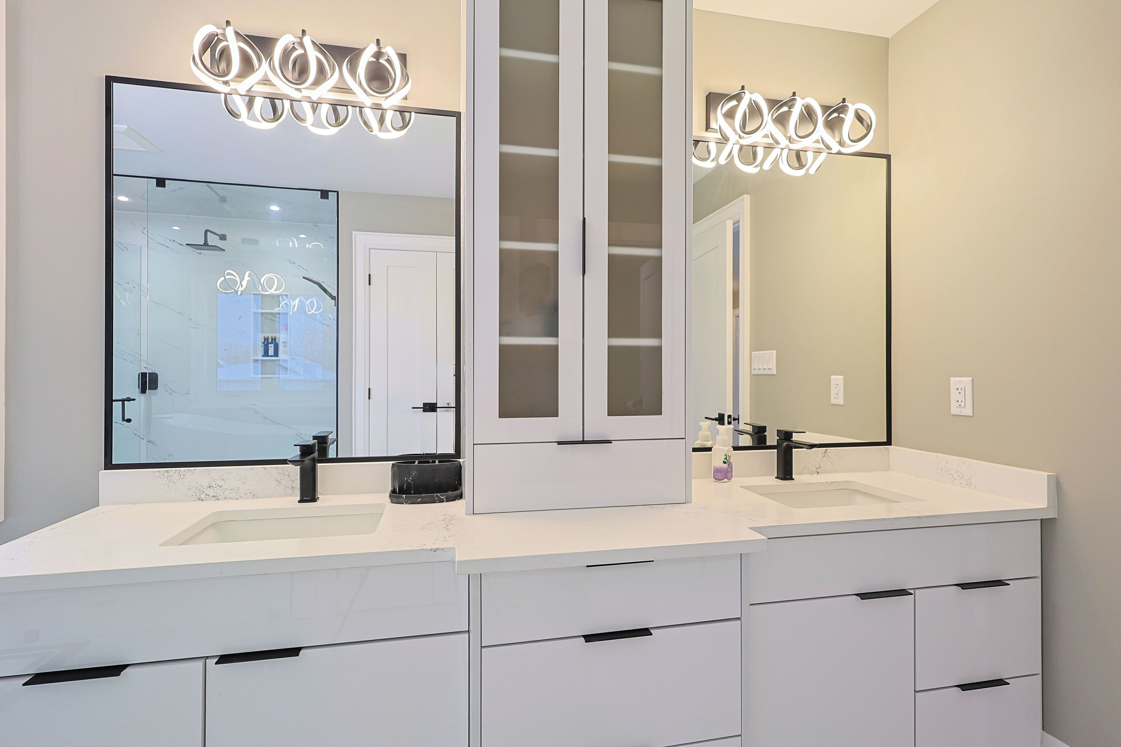 A modern bathroom with two sinks, a large mirror, and a vanity with drawers.