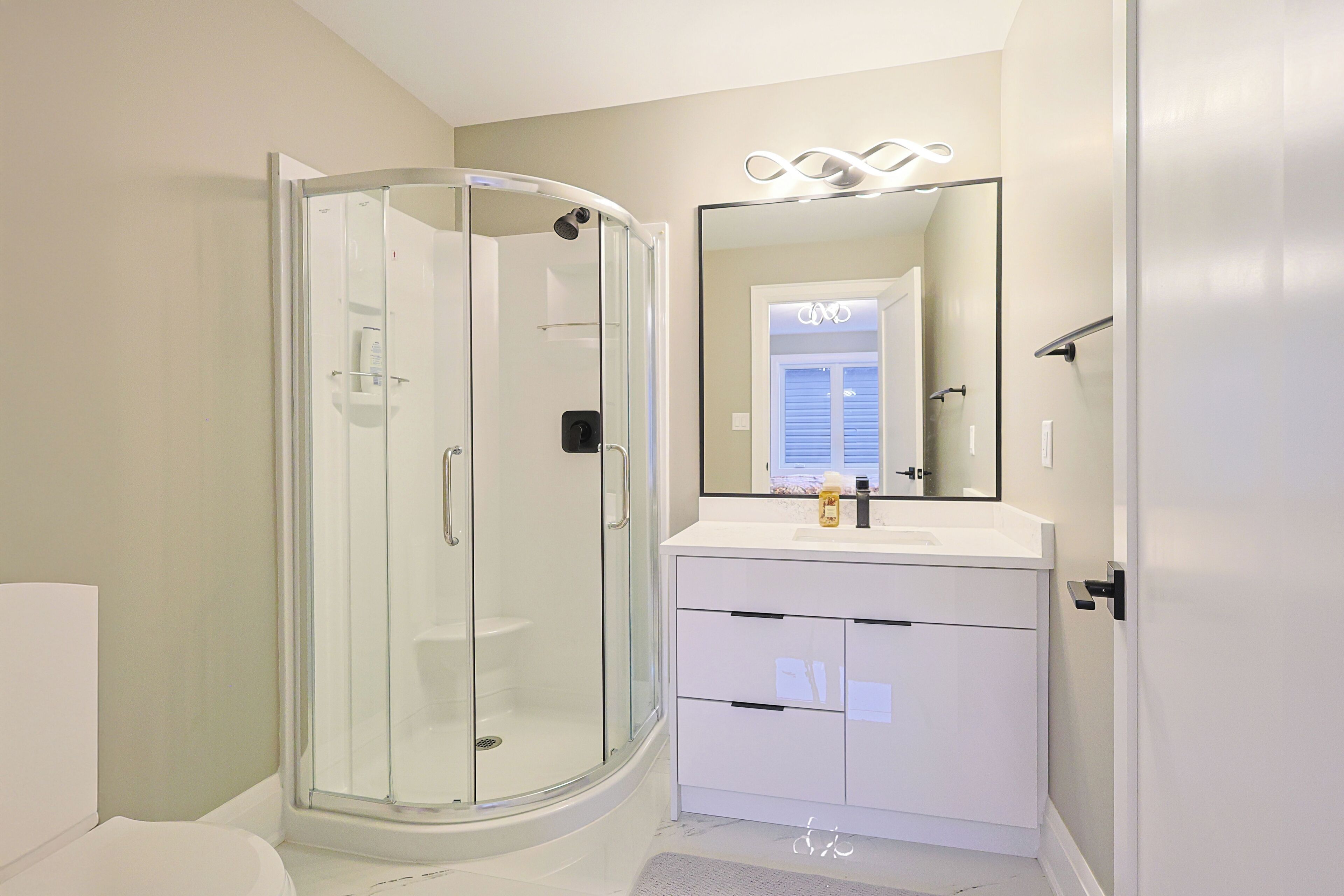 A modern bathroom with a glass-enclosed shower, a white vanity with a mirror, and a toilet.