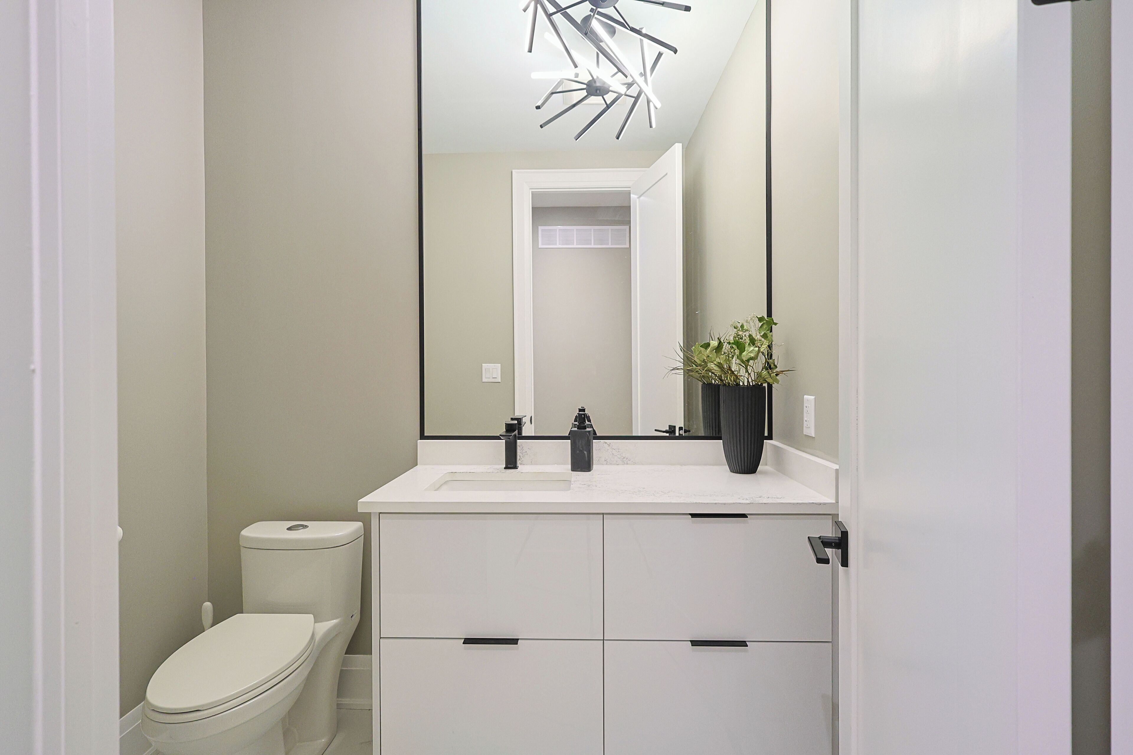 A modern bathroom with a white toilet, a white sink, and a large mirror.