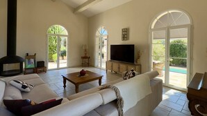 A spacious living room with a sofa, a television, and a fireplace. - Les Lauriers Roses, air-conditioned villa with garden and swimming pool. (L'Isle-sur-la-Sorgue)
