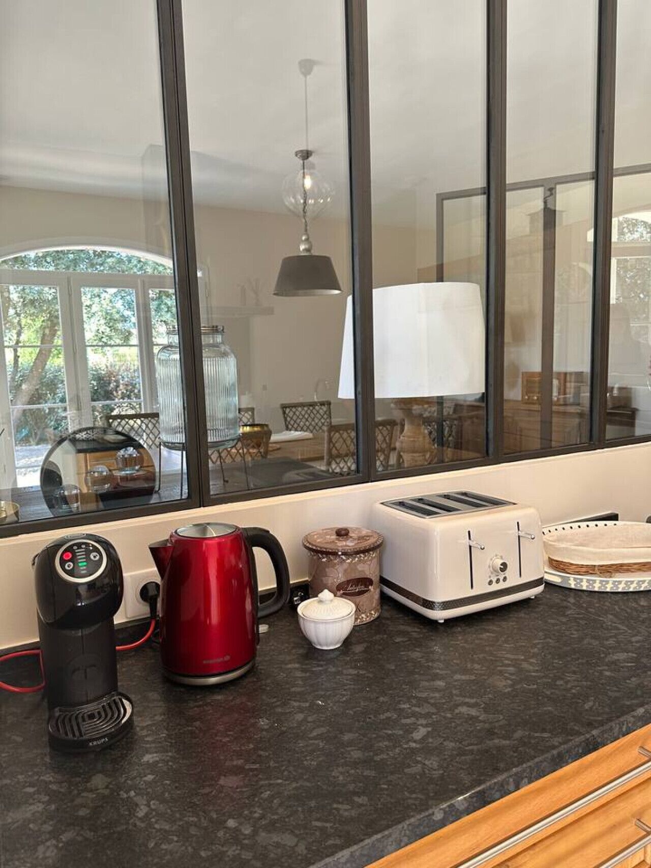 A kitchen with a coffee maker, toaster, kettle, and a window with a view of a dining area.