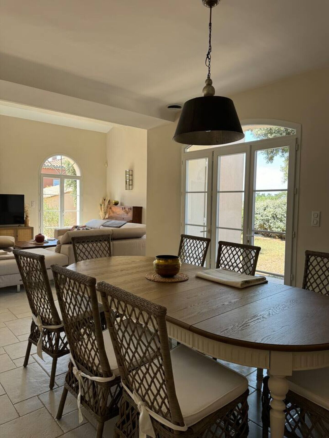 A dining area with a round table, wicker chairs, and a hanging light fixture.