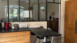 A kitchen with a large window, a dining table with chairs, a toaster, and a kettle. - Les Lauriers Roses, air-conditioned villa with garden and swimming pool. (L'Isle-sur-la-Sorgue)