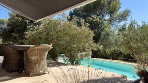 A covered outdoor area with a pool, wicker furniture, and trees. - Les Lauriers Roses, air-conditioned villa with garden and swimming pool. (L'Isle-sur-la-Sorgue)