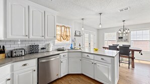 A modern kitchen with white cabinetry, a dishwasher, and a dining area with a wooden table and chairs. - Sleeps 10, Pet-friendly, Fort Rucker (Enterprise)
