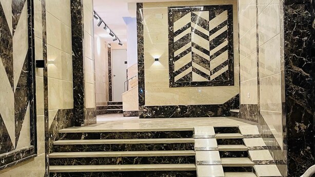 A marble staircase leading to a lobby with a geometric wall design and a chair.