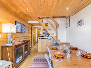 Interior de madeira com uma mesa de jantar posta para quatro, escada e área de cozinha.