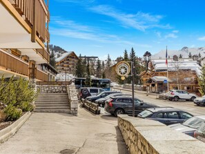 Uma área de estacionamento com carros, um ônibus e um edifício com fachada de madeira e degraus de pedra.