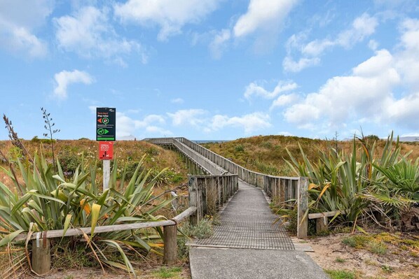 Una pasarela de madera que conduce a una playa, rodeada de vegetación costera.