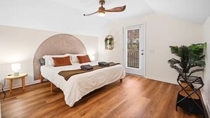 A bedroom with a bed, a ceiling fan, a bedside table, a potted plant, and a door with a window. - The Lazy Lodge: Peaceful Retreat 15 mins from Downtown Greenville (Easley)