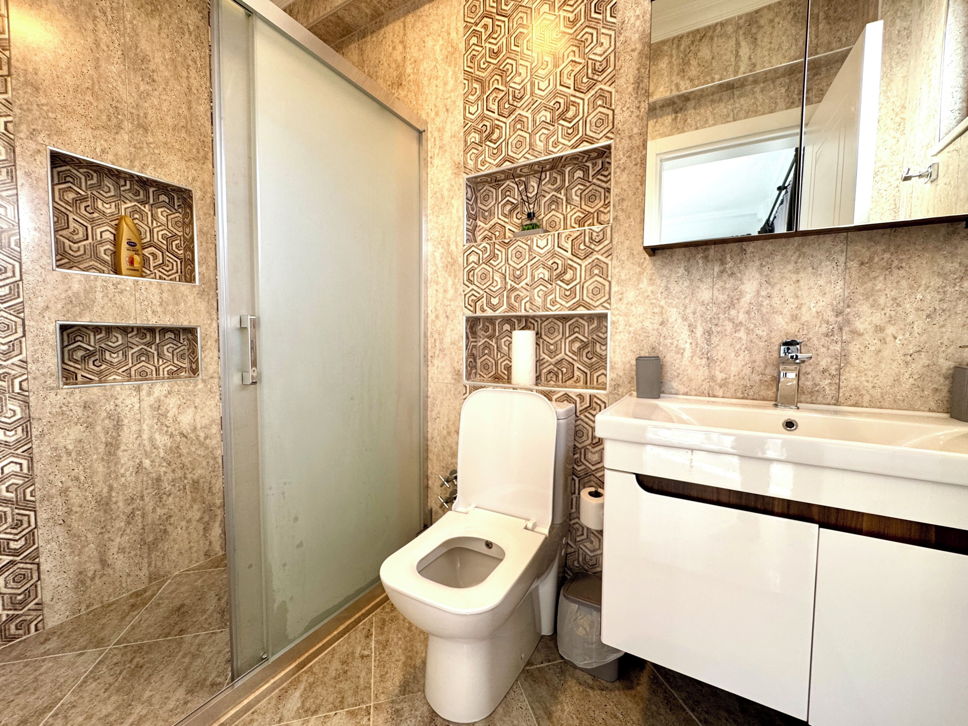 A bathroom with a toilet, sink, and patterned tiles.