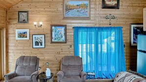 A wooden-paneled room with two armchairs, a sofa, a small table, and a blue curtain.