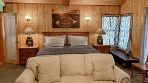 A wooden-paneled room with a bed, two nightstands, a bench, a sofa, and a painting on the wall.