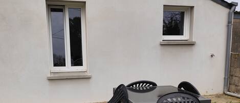 Una casa blanca con dos ventanas, un patio con mesa y sillas, y un césped.