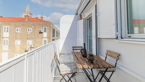 Een balkon met een houten tafel, een bankje en een plant in pot.