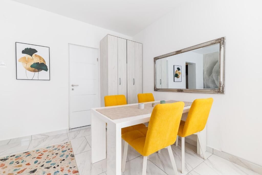 Un comedor con una mesa blanca y sillas amarillas, un armario blanco y un espejo en la pared.
