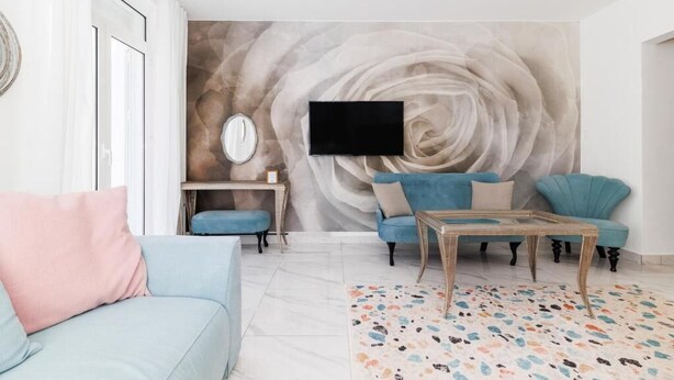 Een woonkamer met een bank, fauteuil, salontafel en een aan de muur bevestigde televisie.