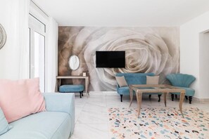 Een woonkamer met een bank, fauteuil, salontafel en een aan de muur bevestigde televisie.