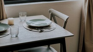 A dining table with plates, glasses, and a candle, set against a window with curtains. - Cozy 1-bedroom apartment in the heart of Tirana (Tirana)