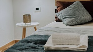 A neatly made bed with a folded towel, a bedside lamp, and a small table with a lamp. - Cozy 1-bedroom apartment in the heart of Tirana (Tirana)