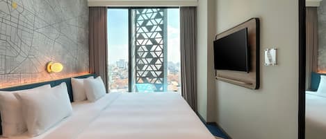 Habitación de hotel con una cama grande, televisión montada en la pared, vista a la ciudad a través de una ventana y un diseño de pared con un mapa.