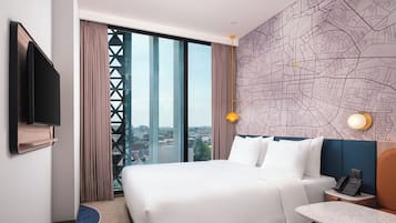 Habitación de hotel con una cama grande, un escritorio, teléfono, televisor y vista a la ciudad.
