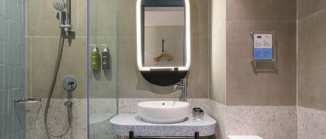 Un baño con ducha de vidrio, un lavamanos blanco con espejo y un perchero para toallas.