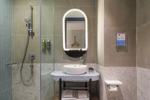 Une salle de bain avec une douche à parois de verre, un lavabo blanc avec un miroir et un porte-serviettes.