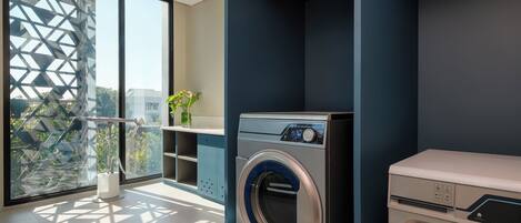 A modern laundry room with a front-loading washing machine, a dryer, and a large window with a geometric view.