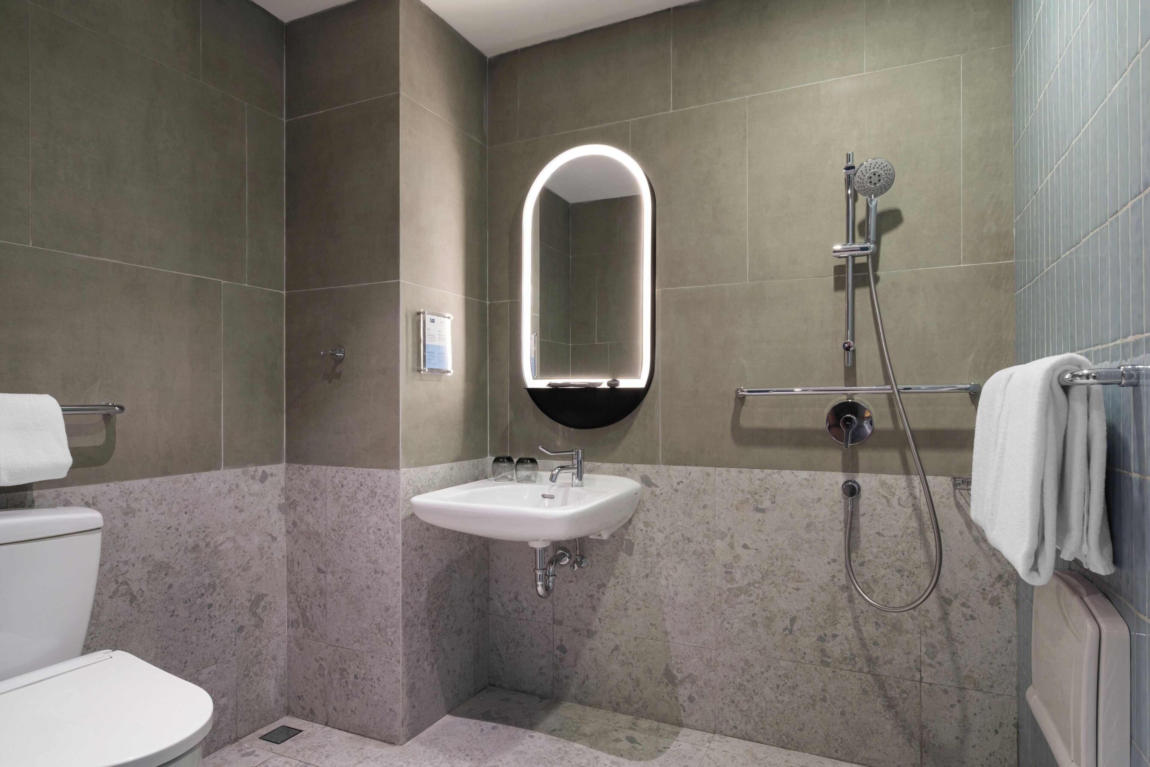 A bathroom with a toilet, sink, shower, and a mirror with a light.