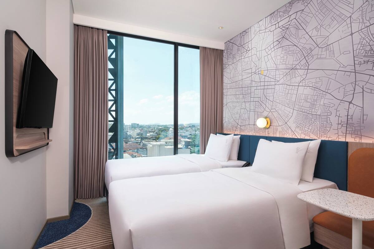 A hotel room with a large window, two beds, a map wall, a TV, and a small table.