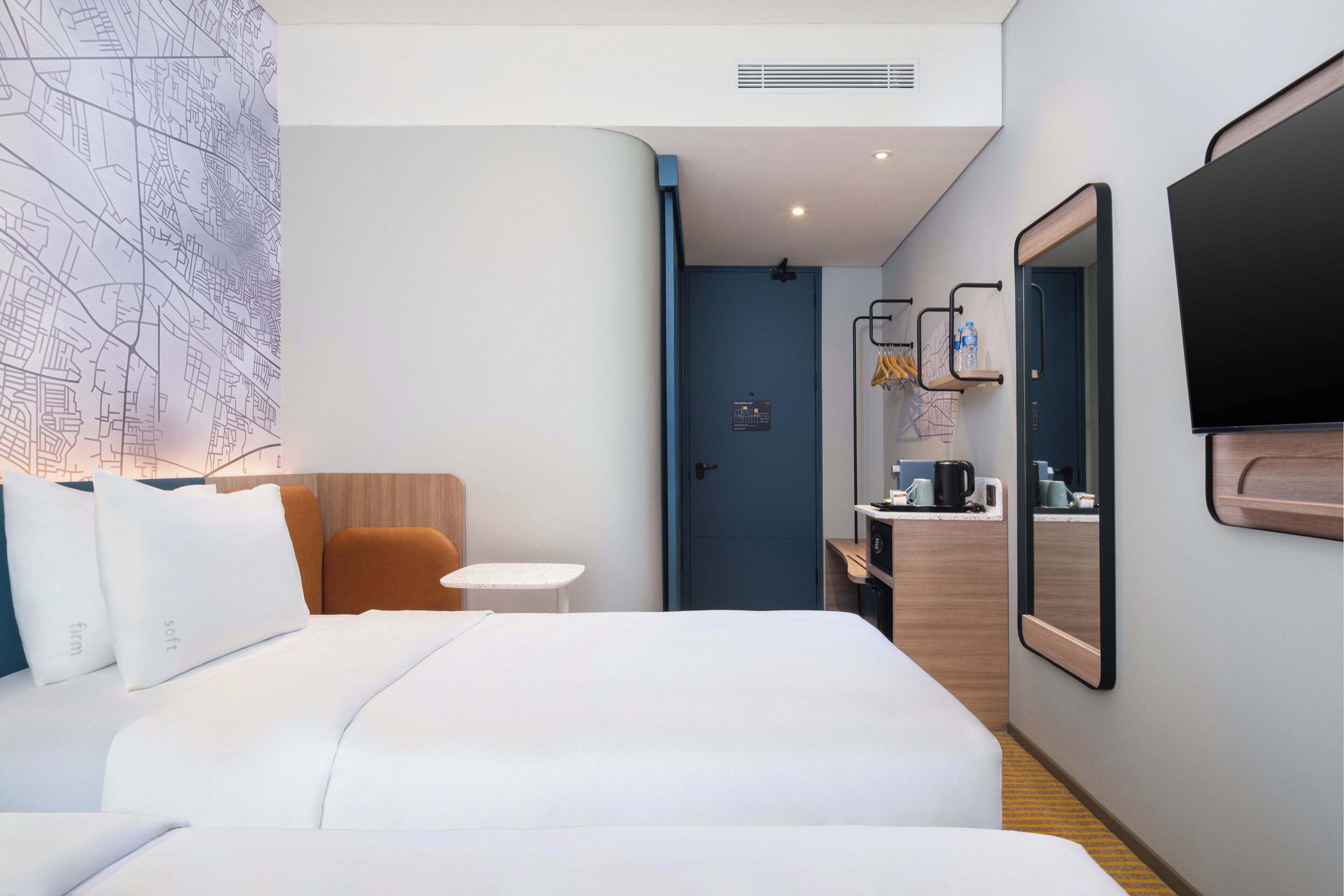 A hotel room with a bed, a small table, a chair, a mirror, a TV, and a door leading to a bathroom.