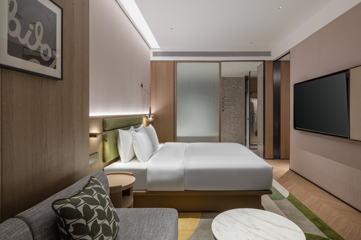 Moderni hotellihuone, jossa on sänky, sohva, televisio ja suihkutila.