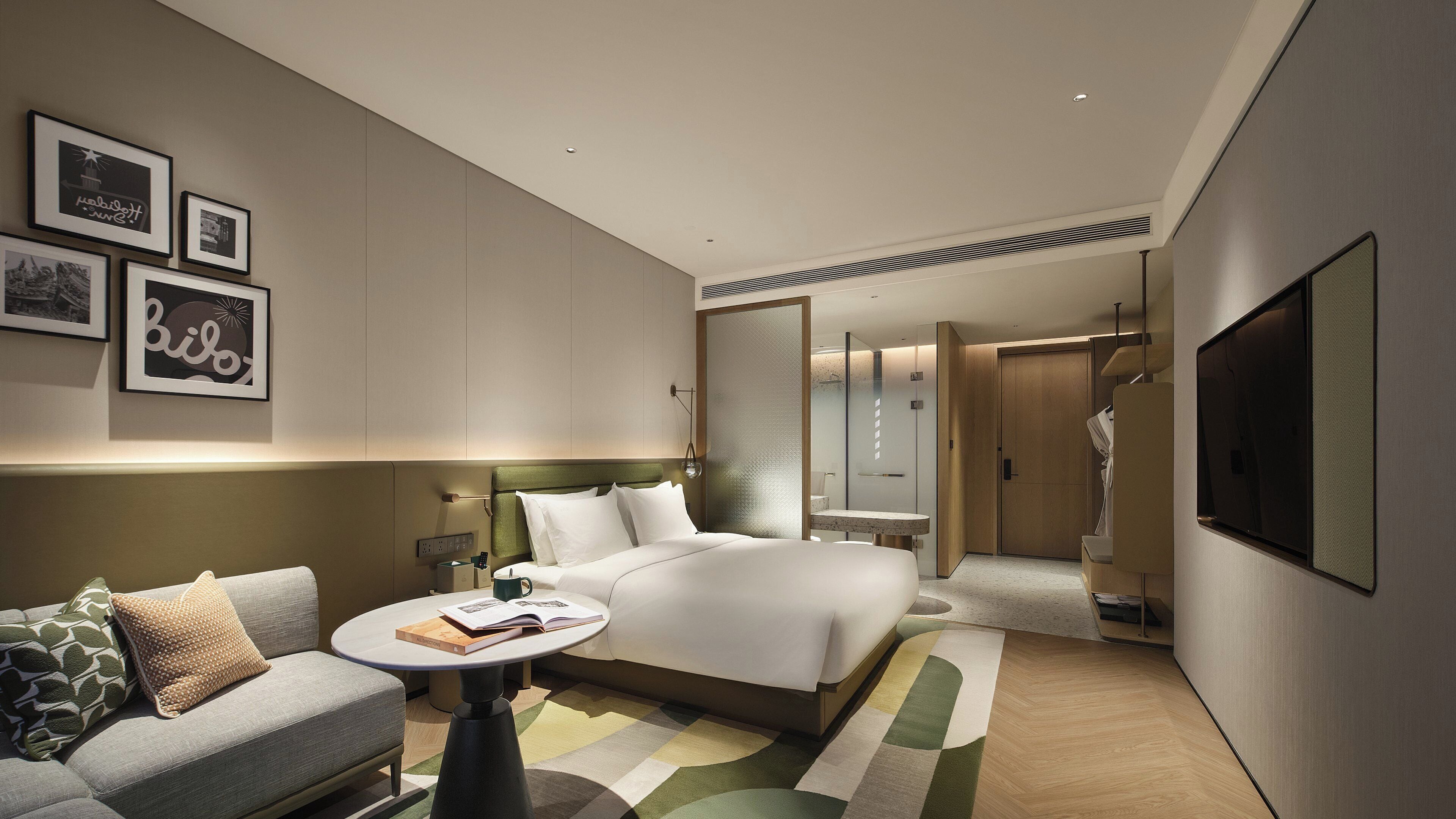 A modern hotel room with a bed, a sofa, a round table, and a TV.