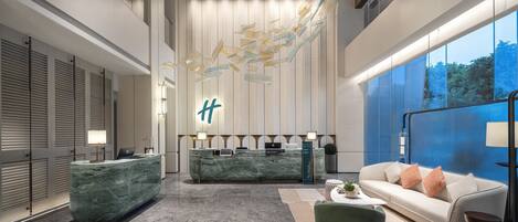 A modern hotel lobby with a reception desk, seating area, and large windows.