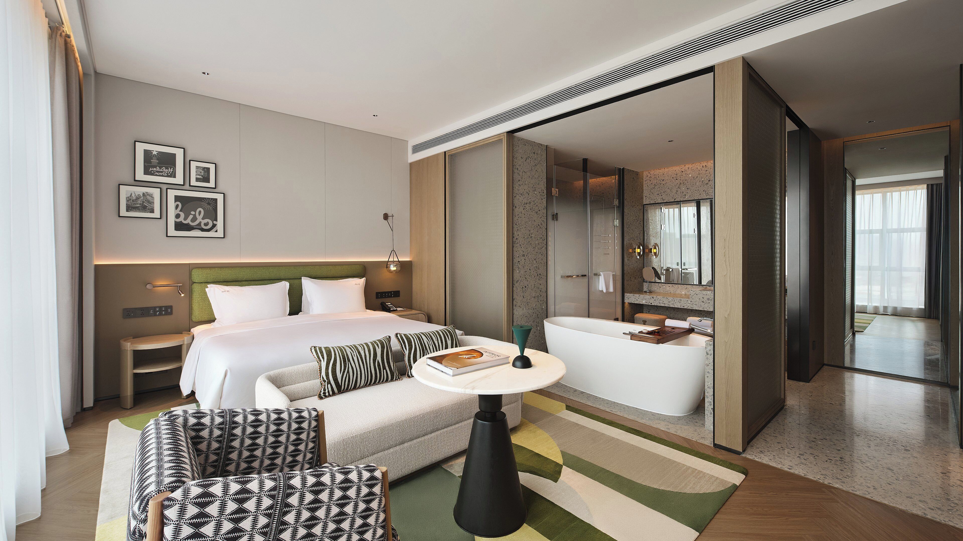 Una habitación de hotel moderna con una cama, un espacio de estar con una mesa, una bañera y un espejo grande.