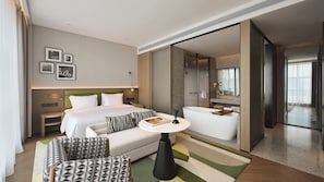 Ett modernt hotellrum med en säng, en sittgrupp med ett bord, ett badkar och en stor spegel.