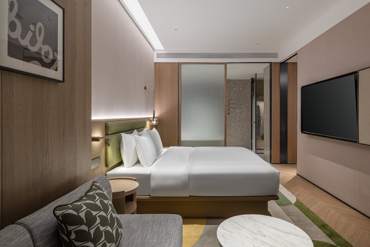 Quarto de hotel moderno com cama, sofá, televisão e área de chuveiro.