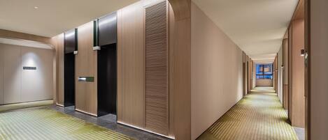 Un pasillo de hotel con diseño moderno, que presenta un largo recorrido con puertas a un lado y suelo alfombrado.