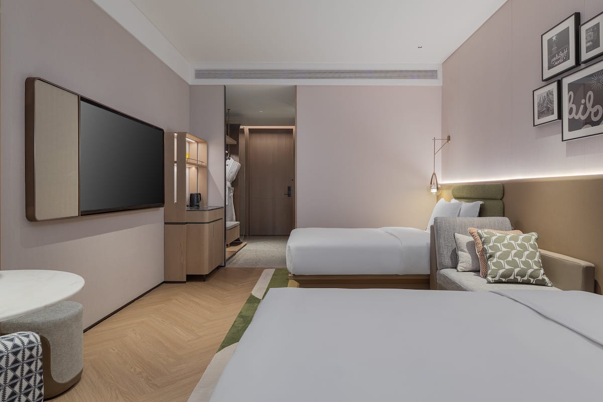 Quarto de hotel com cama, escrivaninha, televisão e banheiro.