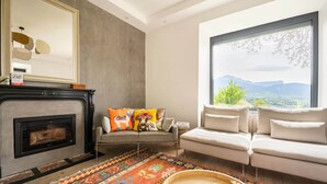 A living room with a fireplace, a sofa, a window with a mountain view, and a patterned rug. - Villa Côte des Vignes x Annecy 15’ (Charvonnex)