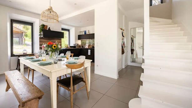 A modern kitchen with white cabinets, a dining area with a wooden bench, and a staircase. - Villa Côte des Vignes x Annecy 15’ (Charvonnex)